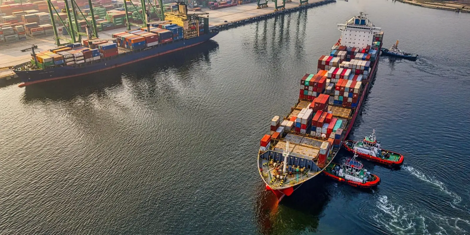 Et containerskip på vei ut av havnen med slepebåter
