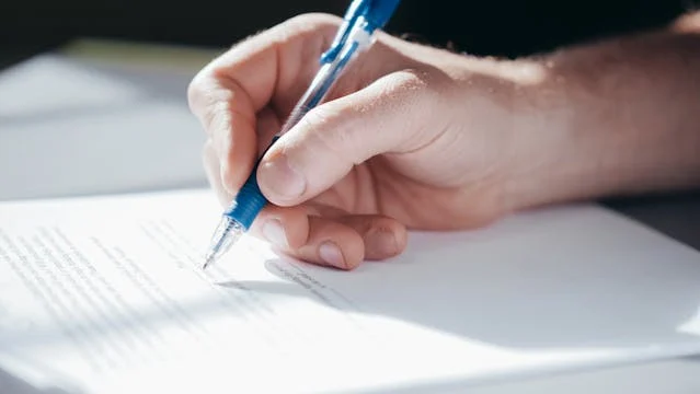 A hand signing a document with a ballpoint pen