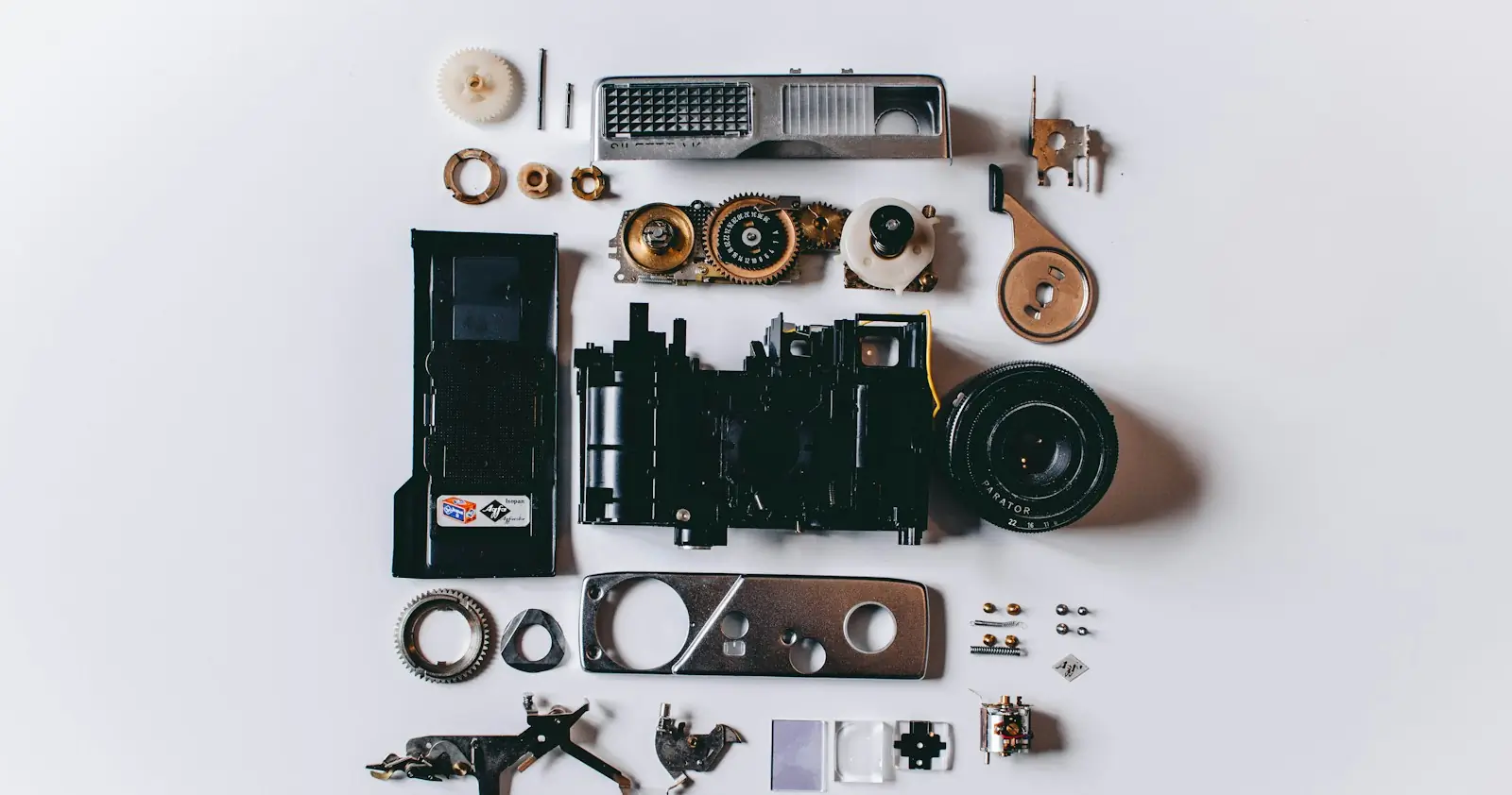 A dismantled camera with all its parts laid out on a white surface